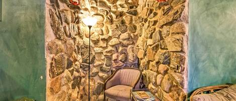 A cozy corner with a stone wall, a chair, a small table, and a floor lamp.