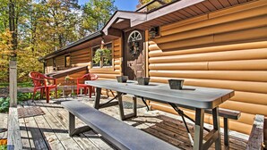 Eine Holzhütte mit einer Terrasse, einem Picknicktisch und roten Stühlen.