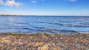 Eine felsige Küste mit klarem, blauem Wasser und einer entfernten Baumgrenze unter einem teils bewölkten Himmel.