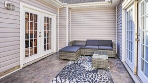 A covered patio with a wicker sofa and ottoman, a patterned rug, and a door with a light fixture. - Prince George Getaway Near Historic Sites! (Prince George)