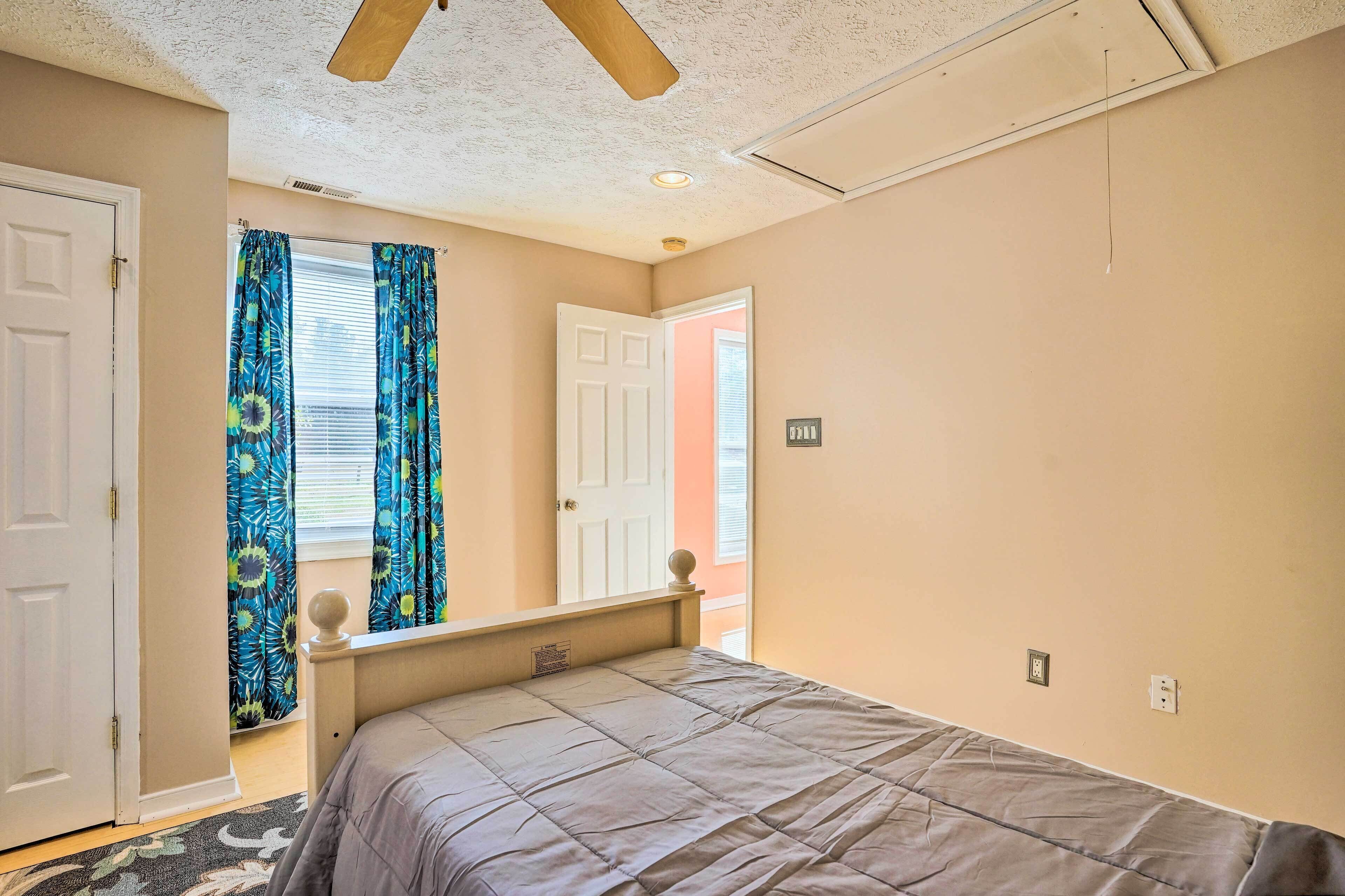 Une chambre à coucher avec un lit, une fenêtre avec des rideaux, une porte et un ventilateur de plafond.