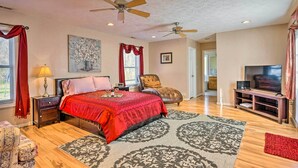 A spacious bedroom with a large bed, two ceiling fans, a TV, and a red accent wall. - Prince George Getaway Near Historic Sites! (Prince George)