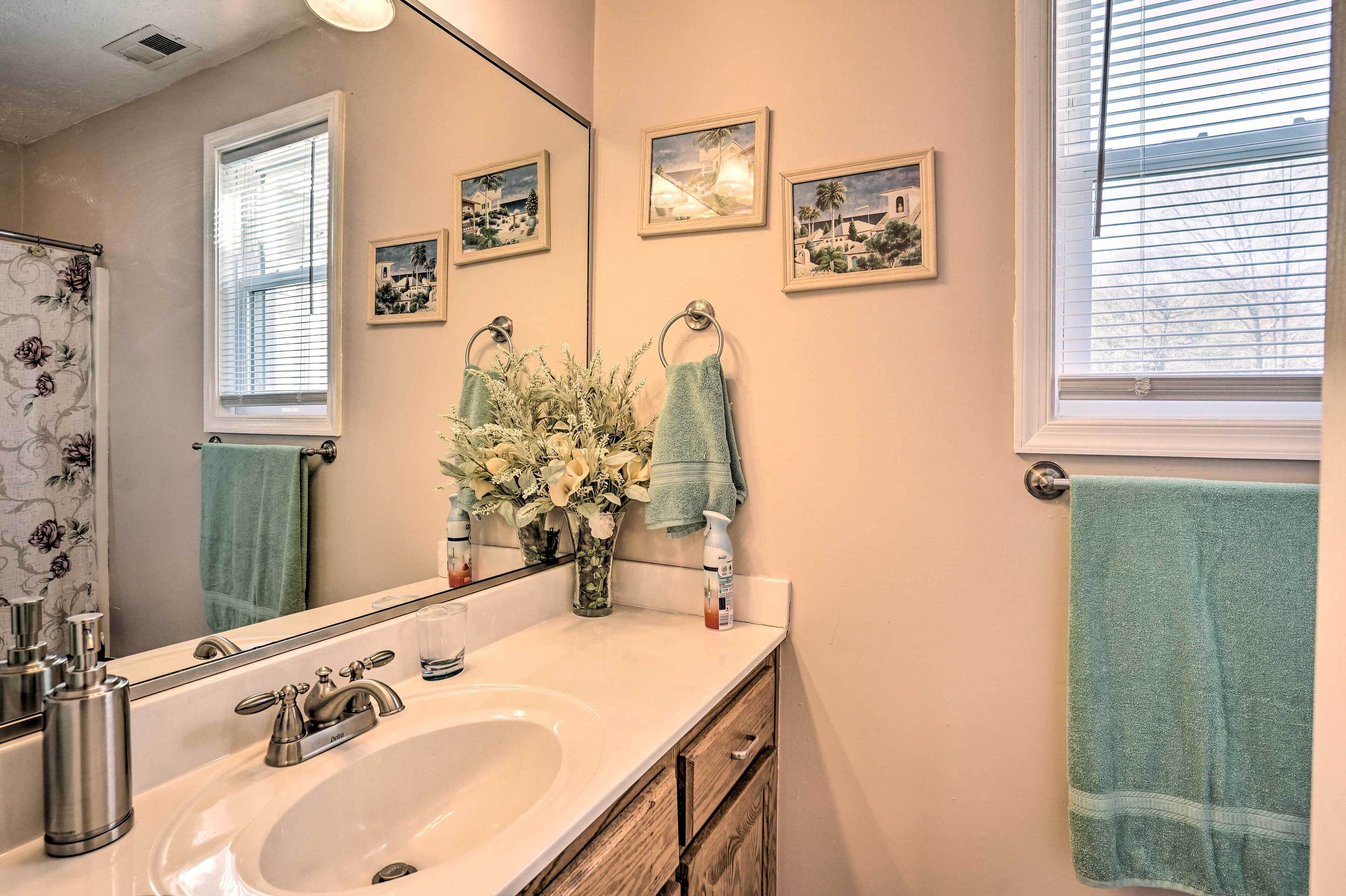 Een badkamer met een witte wastafel, een spiegel, een vaas met bloemen en drie ingelijste foto's aan de muur.