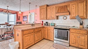 A kitchen with wooden cabinets, a stove, and a dining area with a table and chairs. - Prince George Getaway Near Historic Sites! (Prince George)