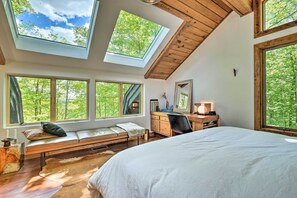 A bedroom with skylights, a large bed, a desk, and a view of trees.