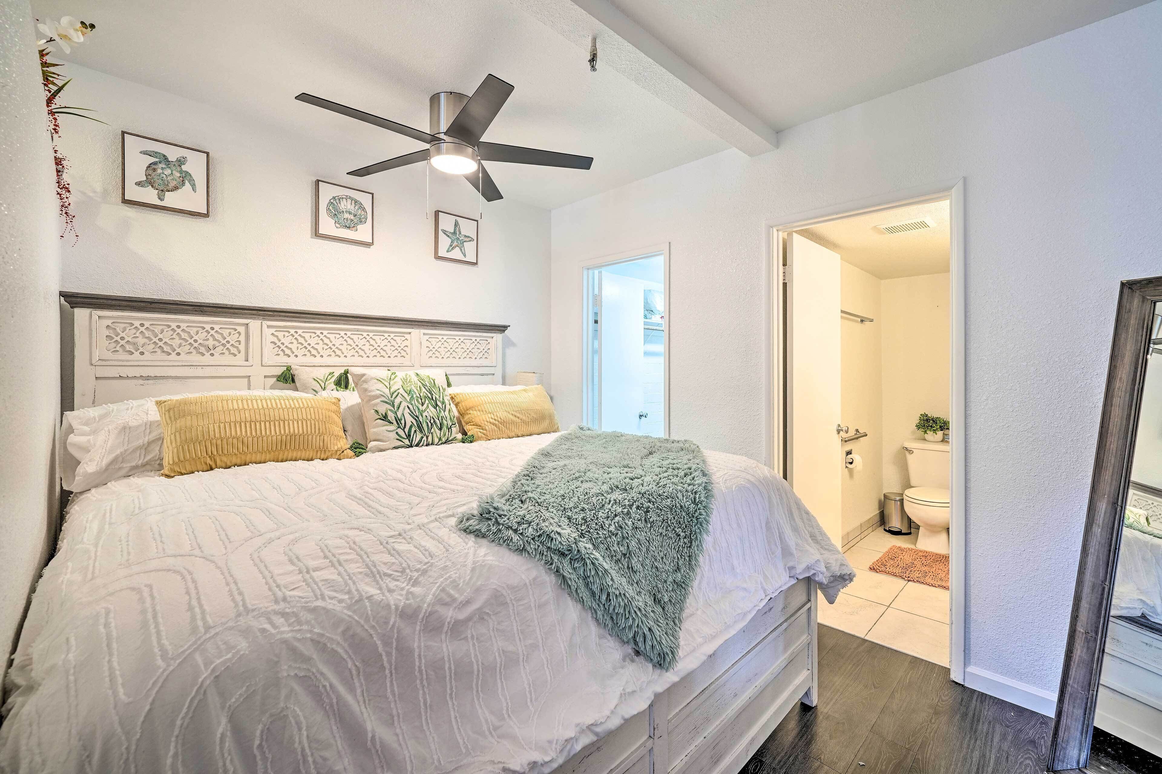 A bedroom with a bed, a ceiling fan, and a view into the bathroom.