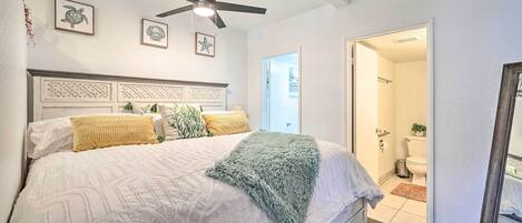 A bedroom with a bed, a ceiling fan, and a view into the bathroom.