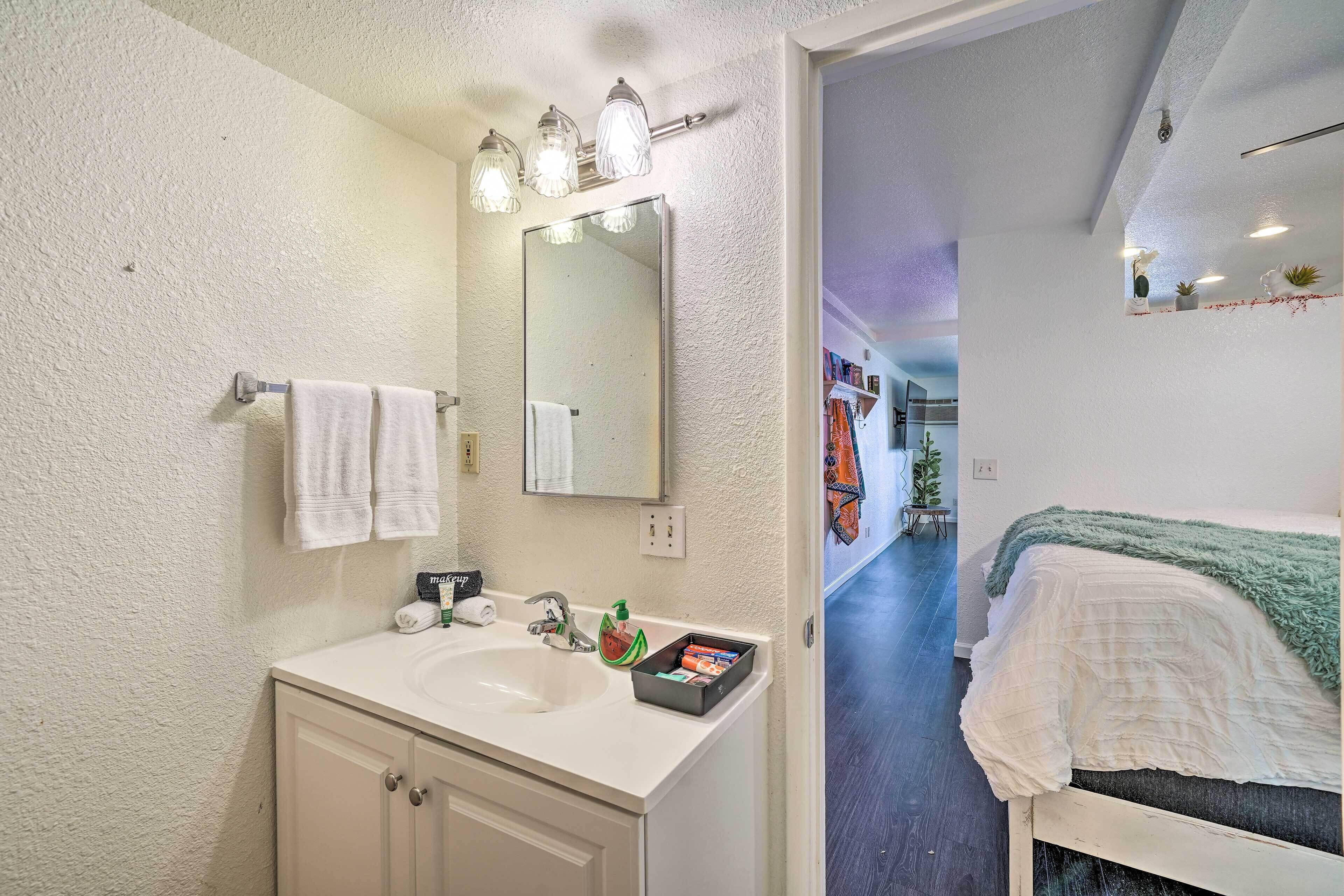 A bathroom with a white sink, mirror, and towel rack. There is a small shelf with toiletries and a box of tissues.