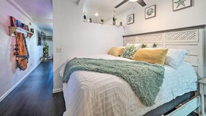 A bedroom with a bed, a ceiling fan, and wall decorations including framed pictures and a shelf with plants. - Parker Studio w/ Patio & Direct River Access! (Parker)