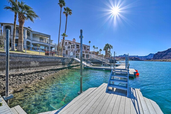A waterfront property with a wooden dock, clear blue water, and a large building with multiple balconies and palm trees. - Parker Studio w/ Patio & Direct River Access! (Parker)