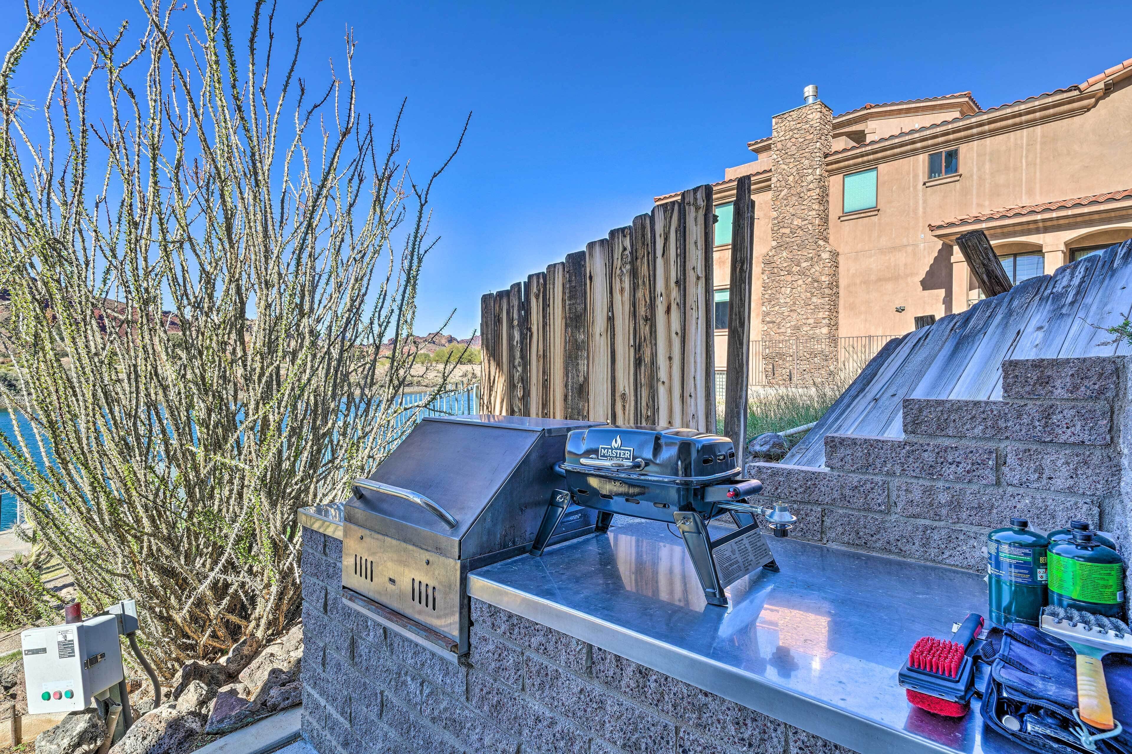 An outdoor grill area with a stone wall, a wooden fence, and a view of a building in the background.