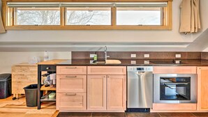 A modern kitchen with wooden cabinets, a stainless steel dishwasher, and an oven. There is a window above the sink and a trash bin to the left. - Updated Boulder Studio ~ 1 Mi to Pearl Street (Boulder)