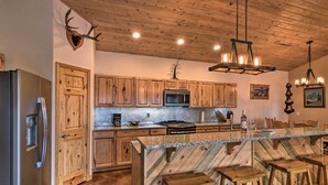 A kitchen with wooden cabinets, a stainless steel refrigerator, a microwave, a stove, and a bar area with stools. - Stunning Home w/ Fire Pit, 11 Mi to Mt Yale! (Buena Vista)