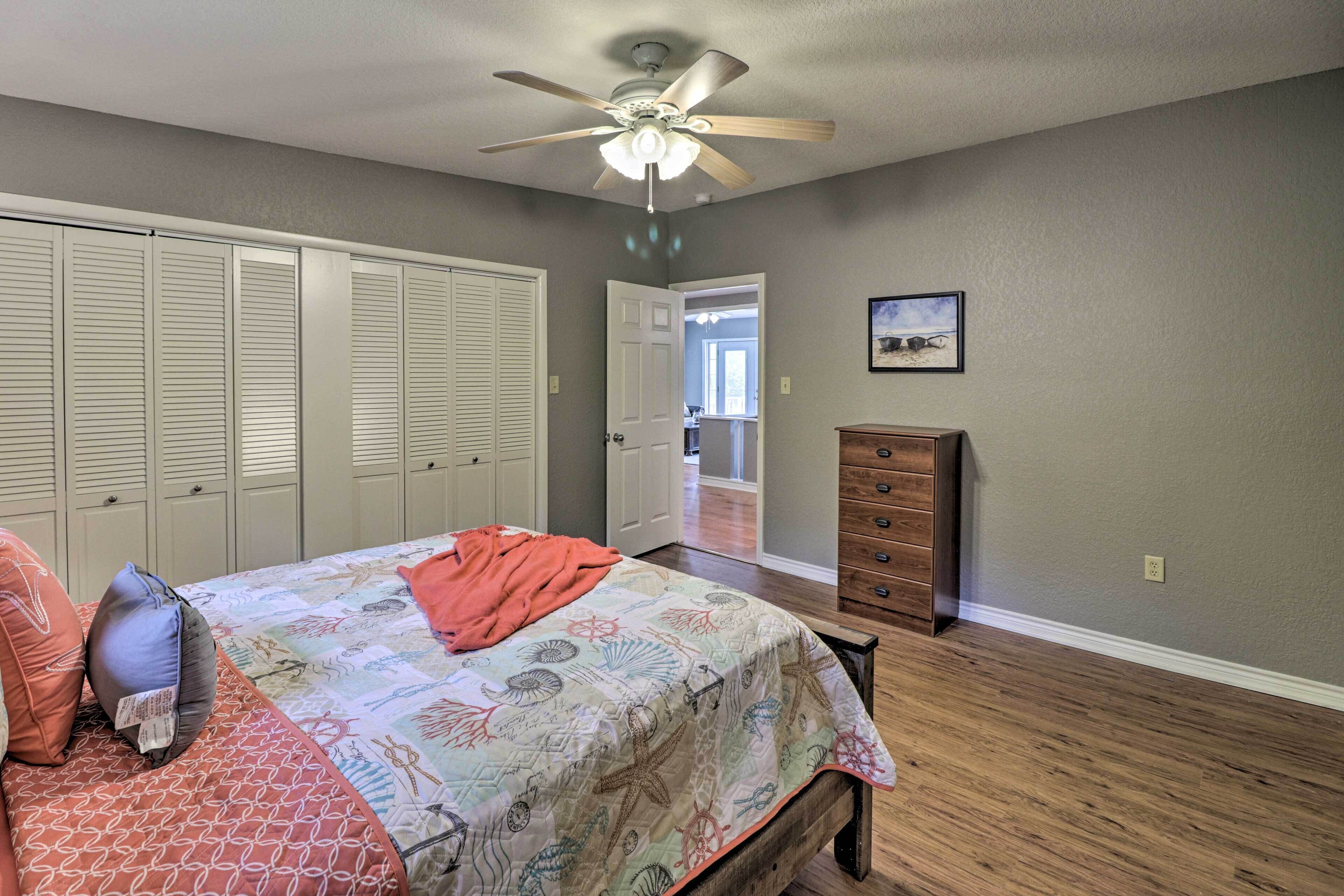 A bedroom with a bed, a ceiling fan, a dresser, and a door leading to another room.