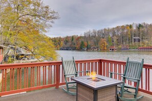A deck with a fire pit and two chairs overlooking a lake with autumn foliage. - Lakefront Zirconia Home w/ Boathouse & Dock! (Zirconia)