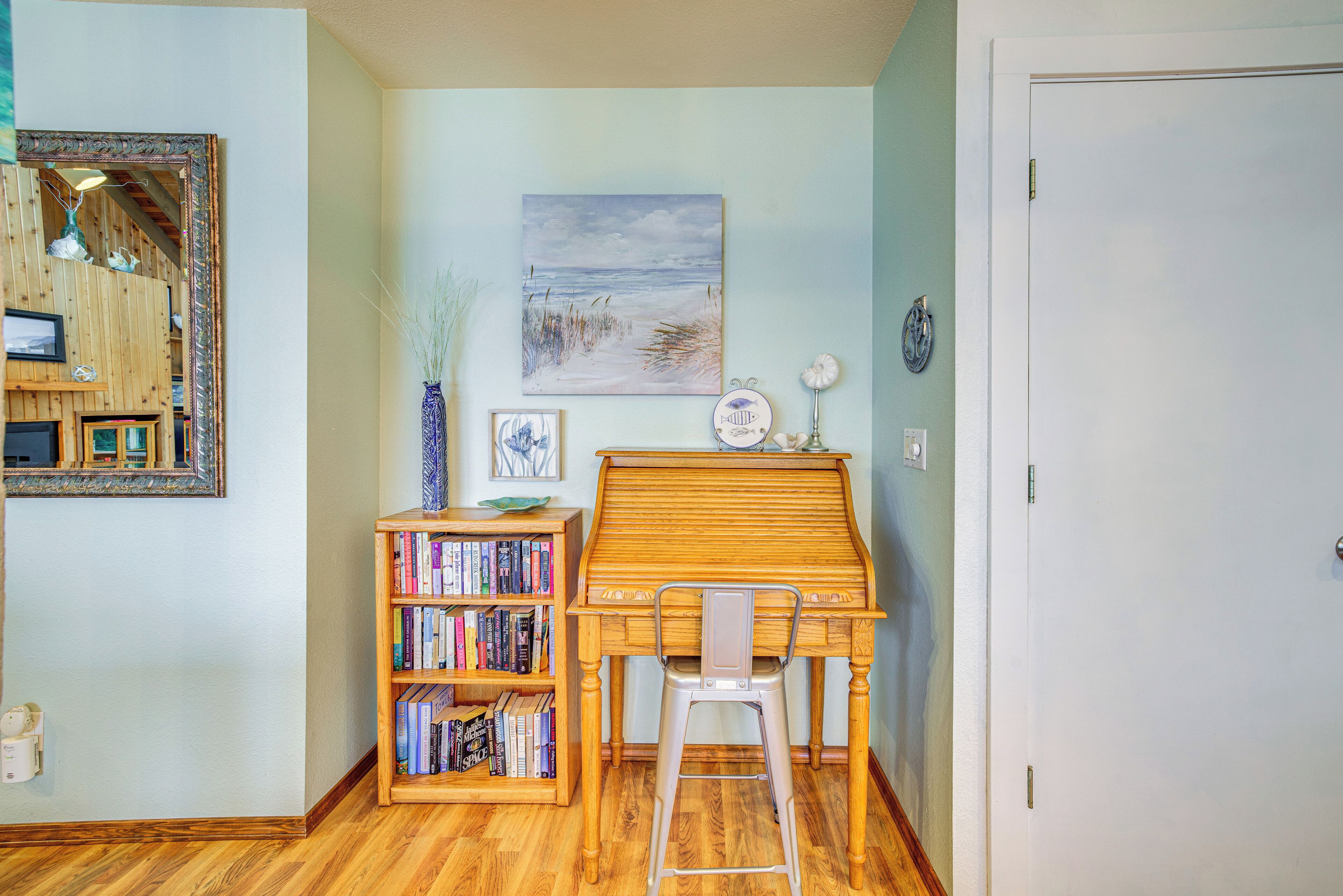 A room with a wooden desk, a bookshelf, a painting, and a door.