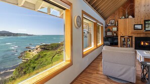 A room with large windows overlooking the ocean, wooden walls, and a fireplace. - Idyllic Coastal Haven - Whale Watch in Depoe Bay! (Depoe Bay)