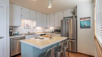 A modern kitchen with white cabinets, stainless steel appliances, a central island with stools, and artwork on the walls.