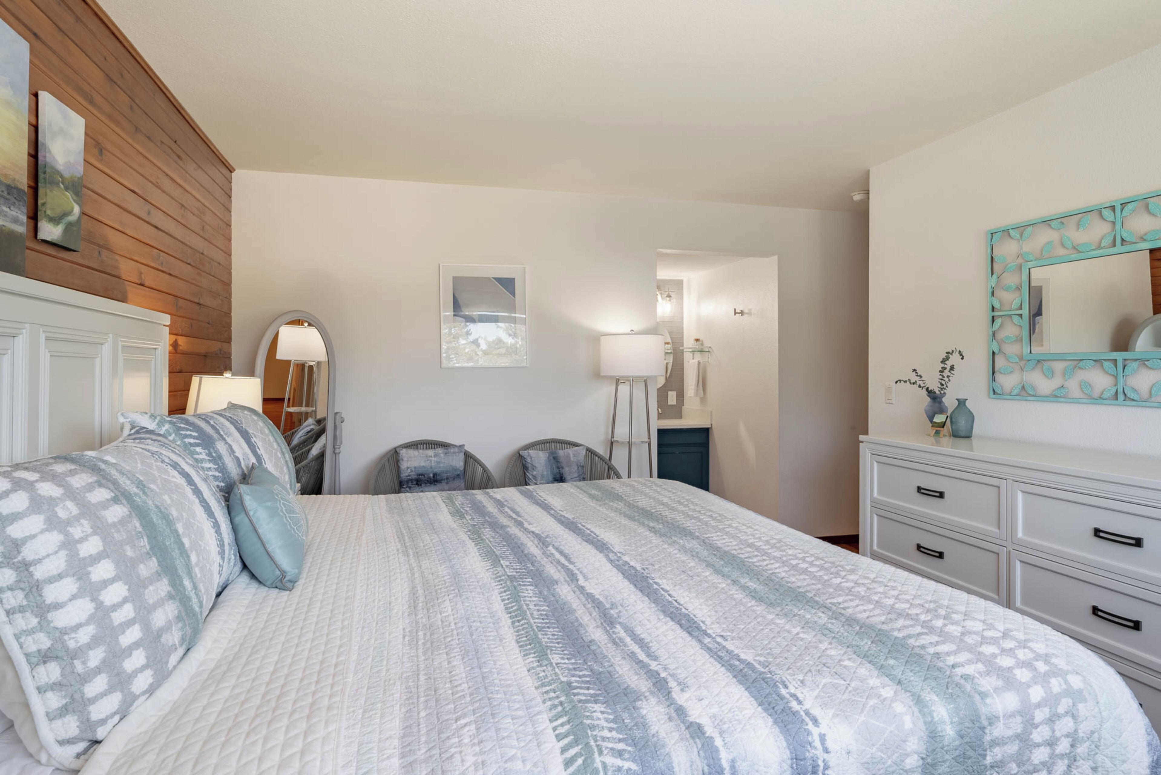 A bedroom with a large bed, a wooden panel wall, a white dresser, and a mirror with a decorative frame.