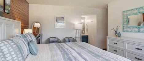 A bedroom with a large bed, a wooden panel wall, a white dresser, and a mirror with a decorative frame.