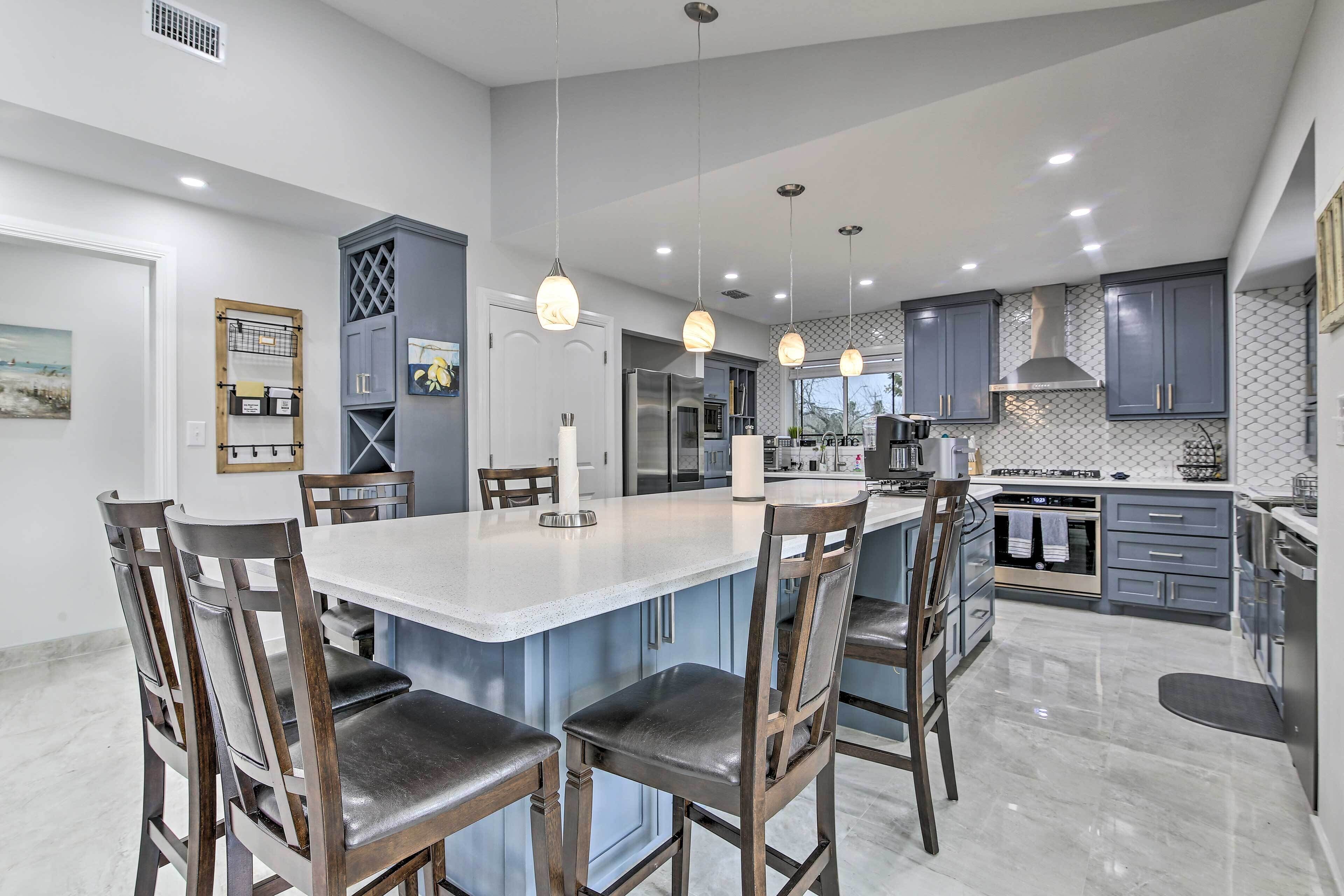 A modern kitchen with a central island, bar stools, pendant lighting, and stainless steel appliances.