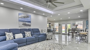 A modern living room with a blue sofa, patterned armchairs, a dining area with a table and chairs, and a ceiling fan. - Patio & Grill: Spacious Gem Near Gulf Coast! (Brownsville)