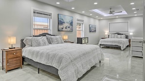 A modern bedroom with a large bed, bedside tables, a ceiling fan, and artwork on the walls. - Patio & Grill: Spacious Gem Near Gulf Coast! (Brownsville)