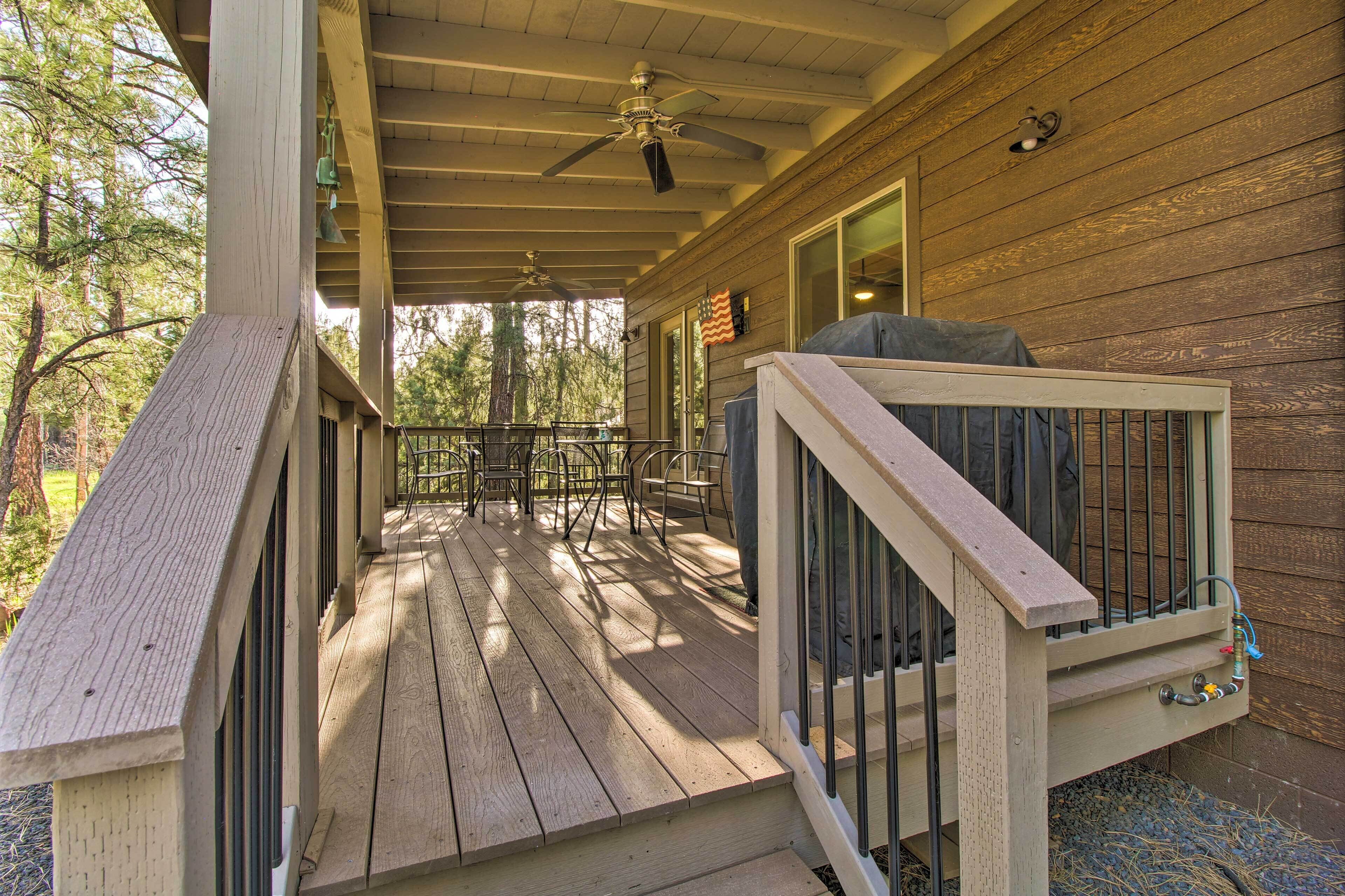 A wooden deck with a railing, a ceiling fan, and a patio table with chairs.