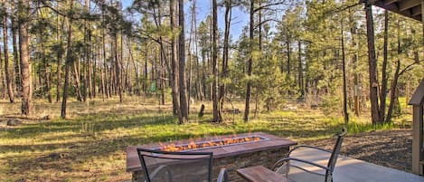 An outdoor patio with a fire feature, seating, and a view of a forest.