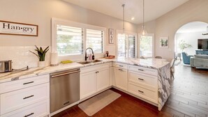 A modern kitchen with white cabinetry, a built-in dishwasher, and a large window with blinds.