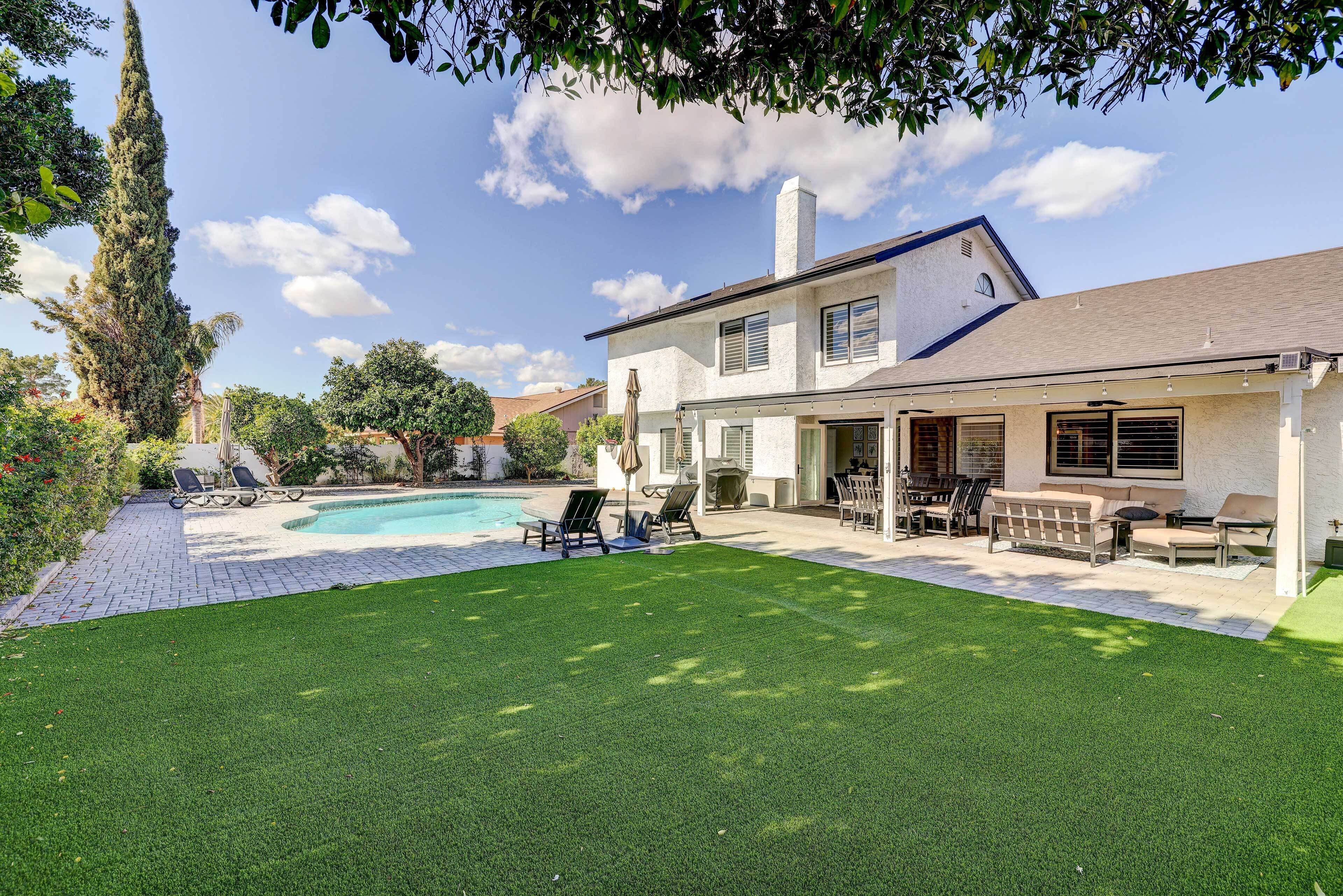 A two-story house with a swimming pool, outdoor seating, and a well-maintained lawn.