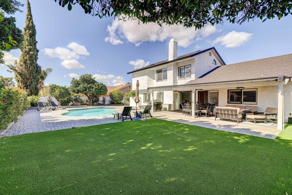 A two-story house with a swimming pool, outdoor seating, and a well-maintained lawn.