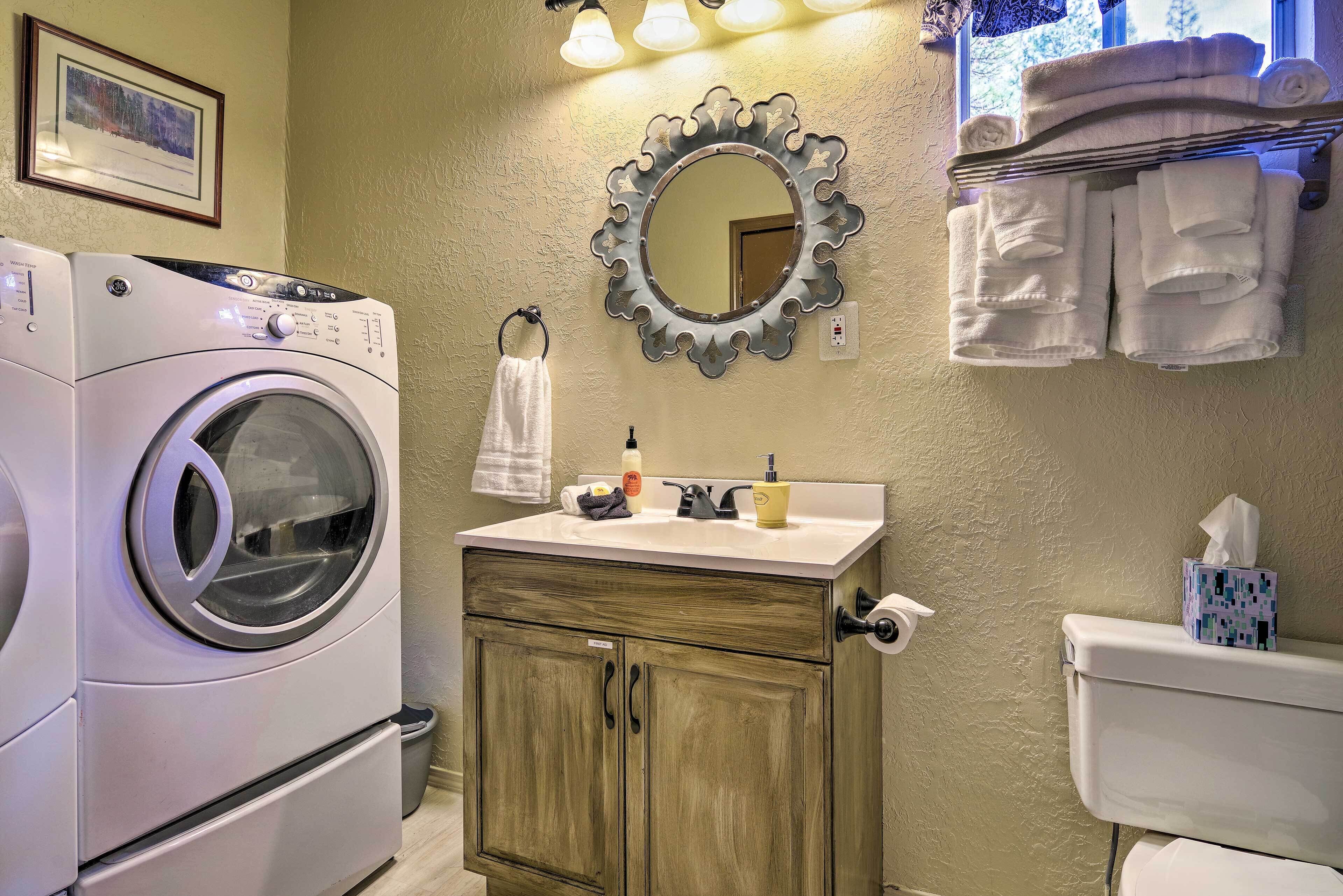 Un espace buanderie comprenant un lave-linge, un évier avec des articles de toilette et des serviettes suspendues sur un étendoir.