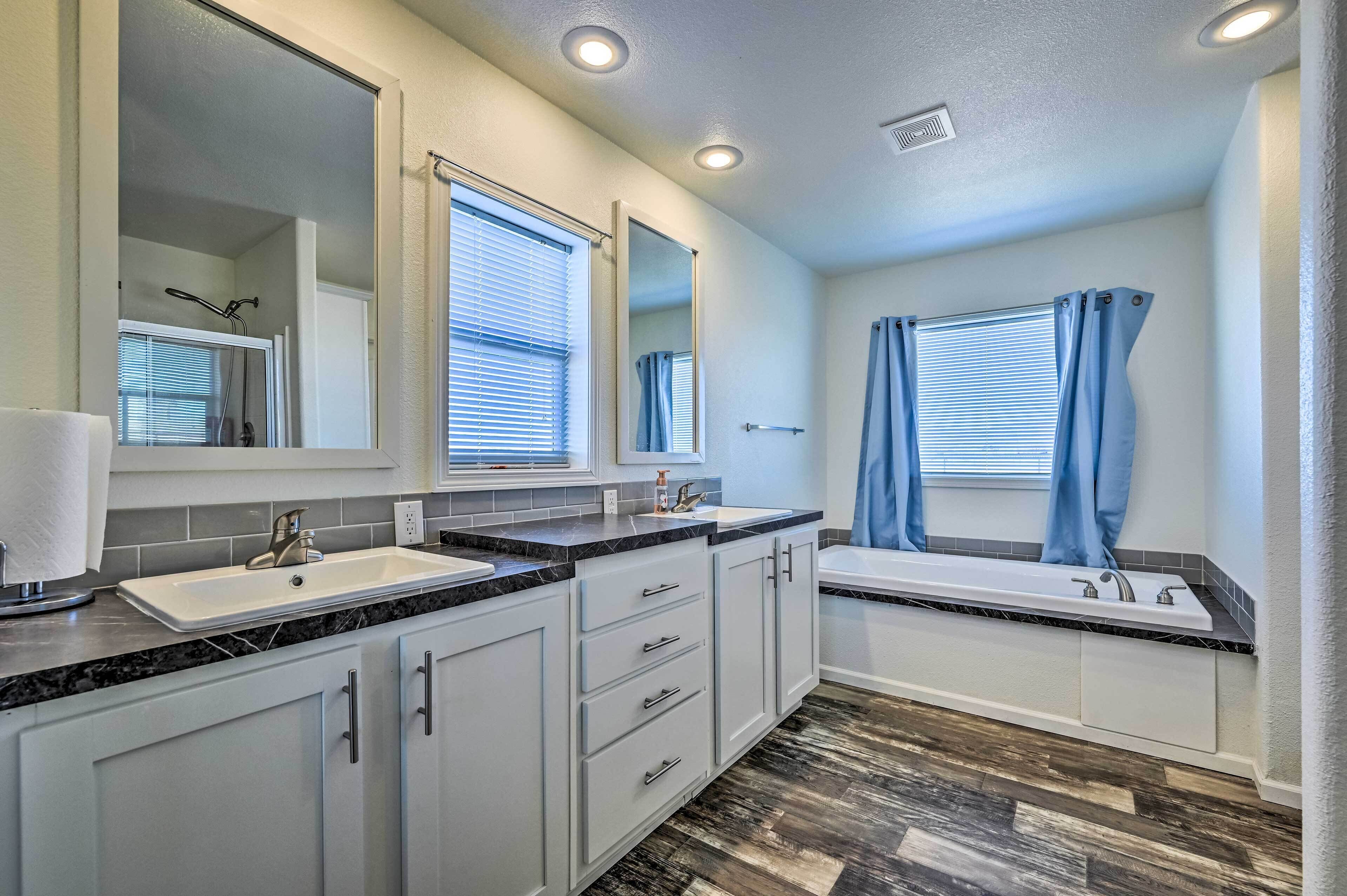 A modern bathroom with two sinks, a bathtub, and a large mirror.