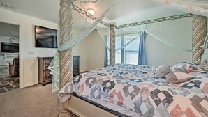 A bedroom with a four-poster canopy bed, a television mounted on the wall, and a dresser.