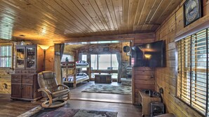 A wooden cabin interior with a rocking chair, a television, and a fireplace.