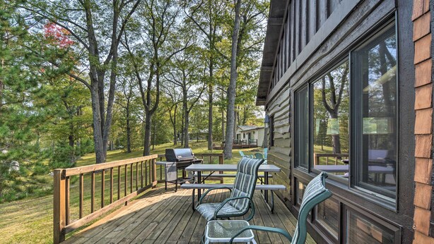 A wooden deck with outdoor furniture, a grill, and a view of a forested area.