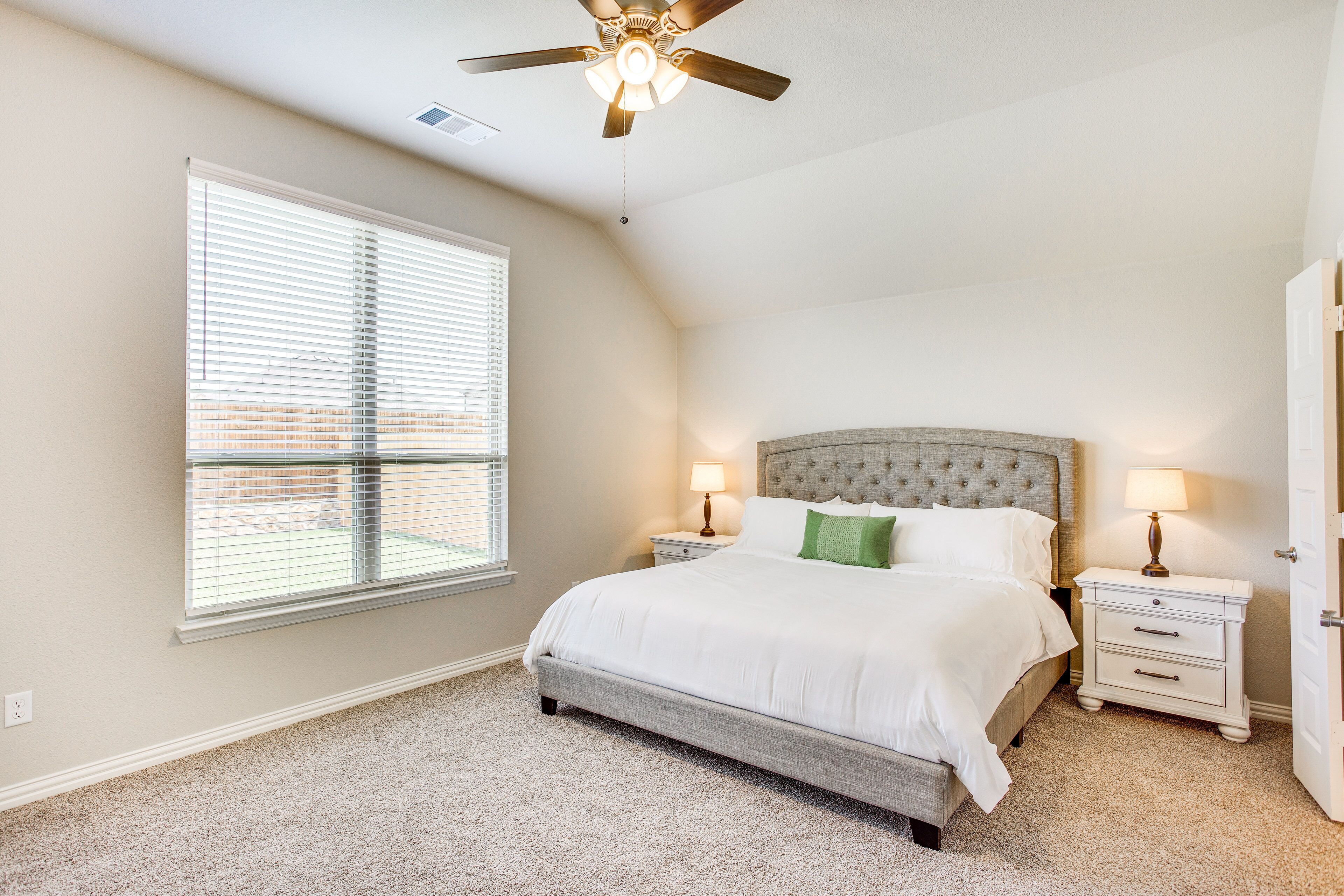 A bedroom with a bed, two bedside tables, a ceiling fan, and a window with blinds.