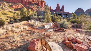 Une maison moderne, située dans un paysage désertique, entourée de formations rocheuses rouges et d’une végétation clairsemée.