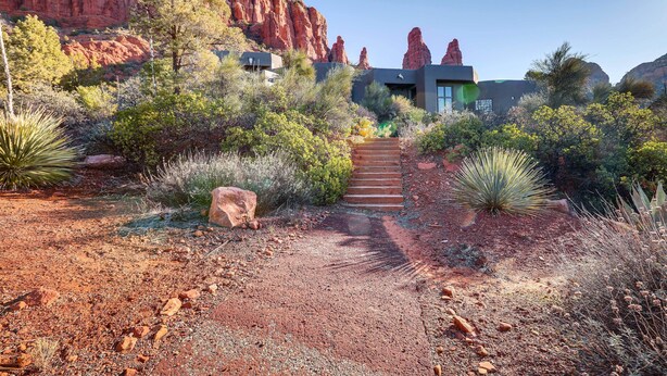 Un paysage désertique avec un bâtiment moderne doté d’un escalier menant à une porte, le tout entouré de cactus et de formations rocheuses rouges.
