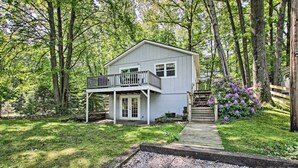 Une maison à deux étages avec un balcon, entourée d’arbres et dotée d’une terrasse en bois.