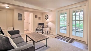 Un salon comprenant un canapé, une table basse, une lampe et donnant sur un jardin grâce à de grandes portes vitrées.