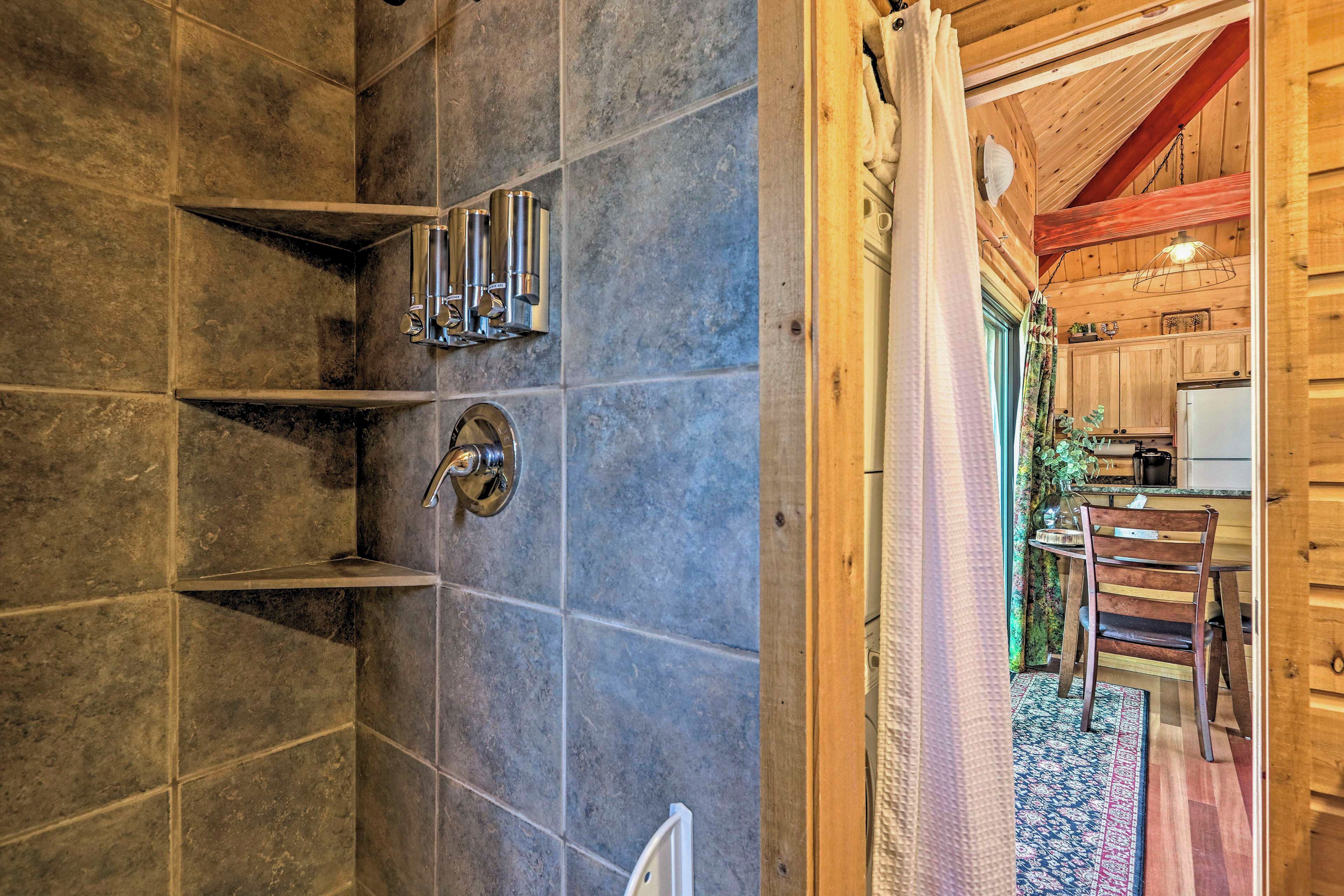 Ein Badezimmer mit Dusche, Waschbecken und Toilette. Holzdecke und ein Fenster mit Vorhängen.