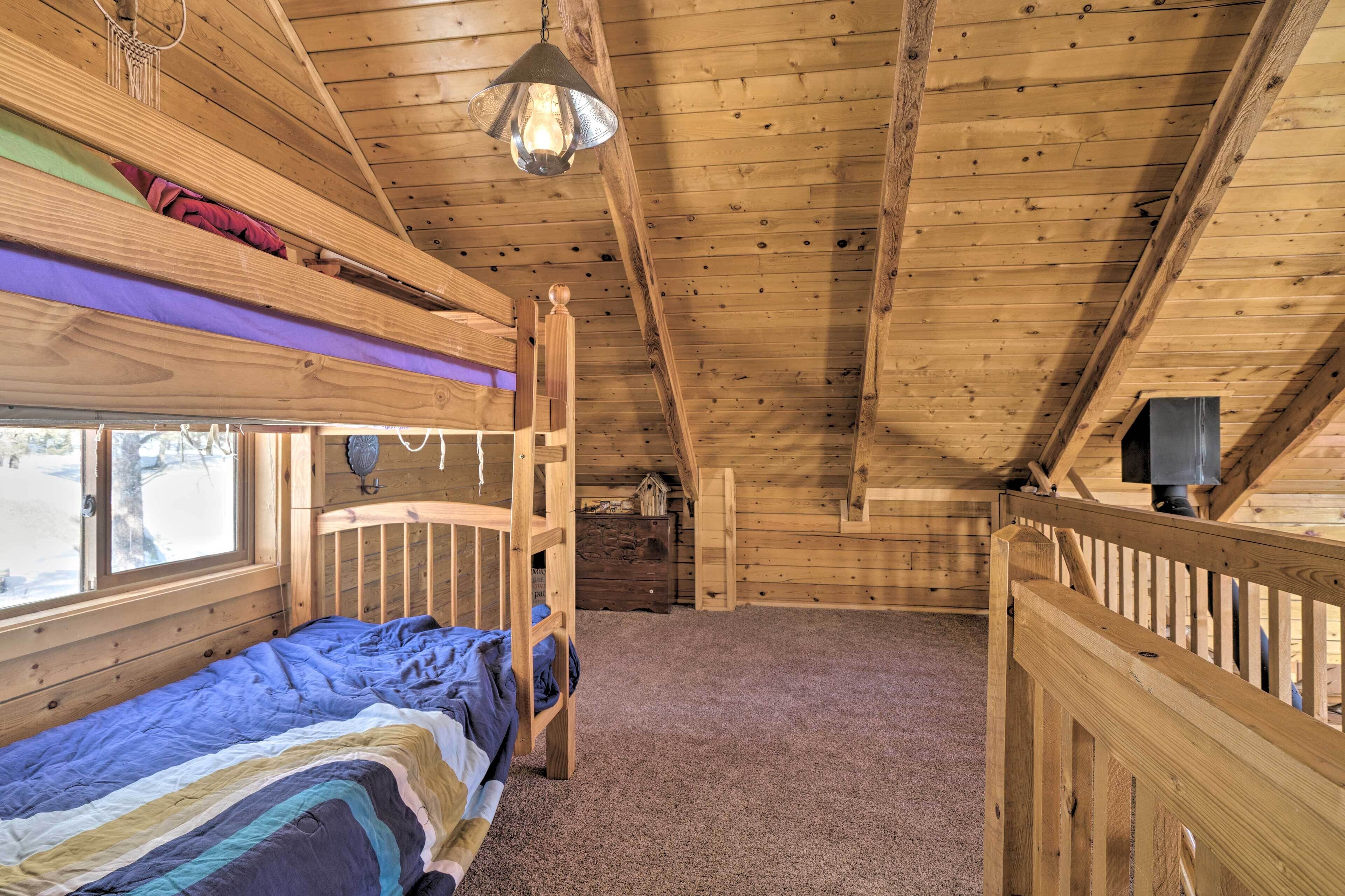 A cozy attic bedroom with a bunk bed, a small desk, and a window overlooking a snowy landscape.