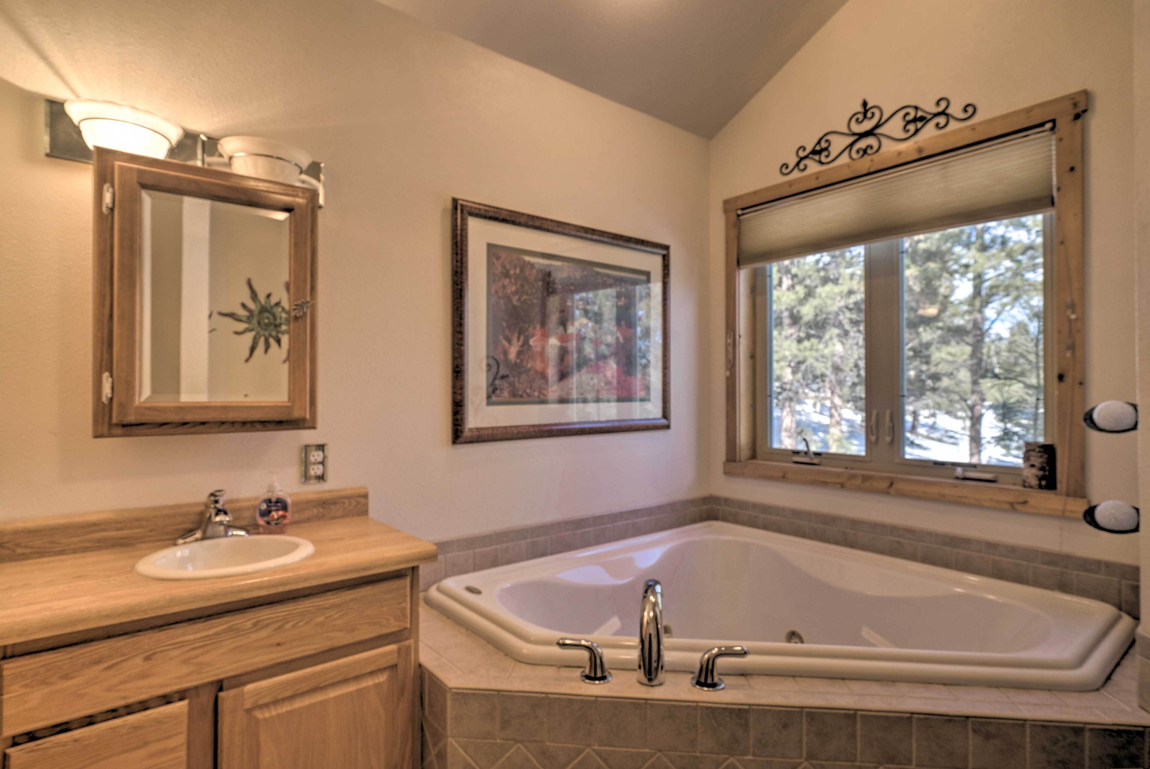 A bathroom with a bathtub, a sink, and a window with a view of trees.