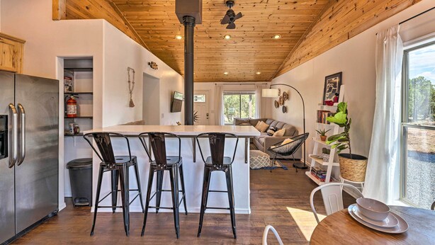A modern kitchen with a central island, bar stools, and a dining table with plates. - 1 Mi to Hiking: Chic Show Low Escape w/ Fire Pit! (Show Low)