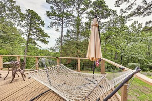 A hammock on a wooden deck with a table and chairs, surrounded by trees.