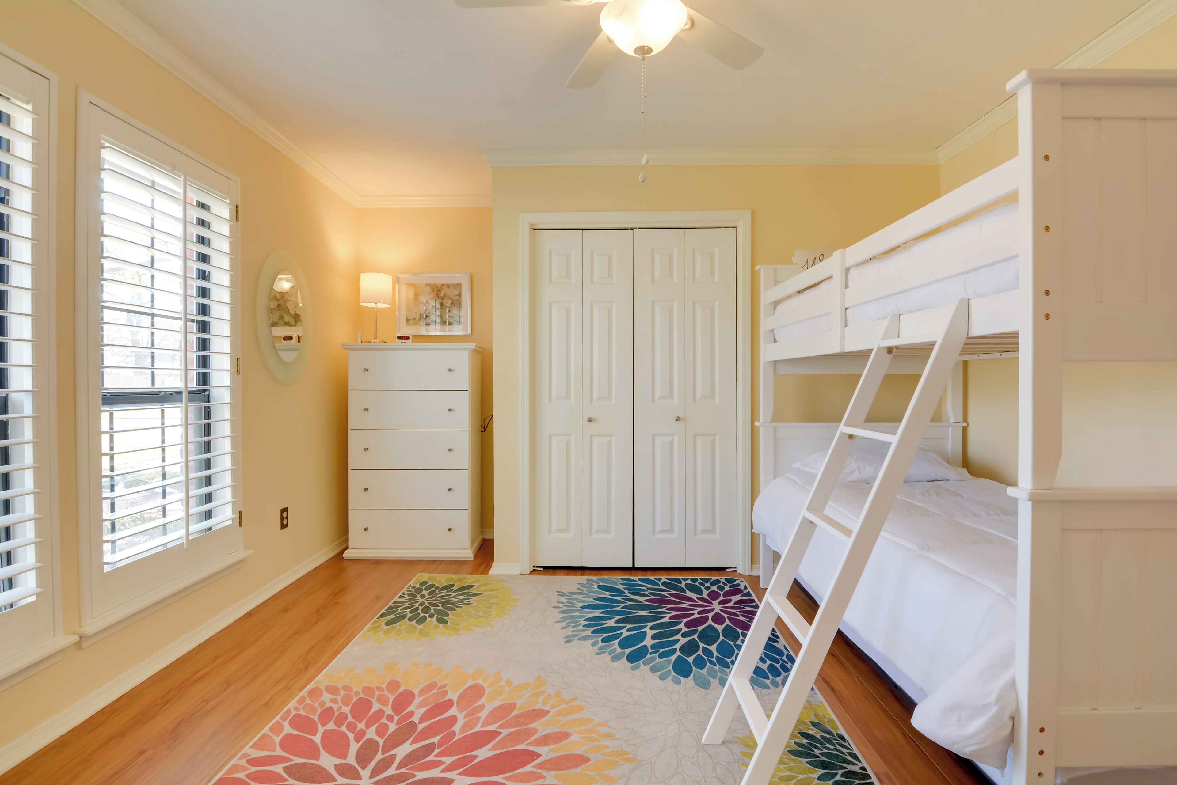 A bedroom with a bunk bed, a dresser, a door, and a window with blinds.