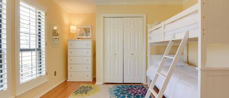 A bedroom with a bunk bed, a dresser, a door, and a window with blinds.