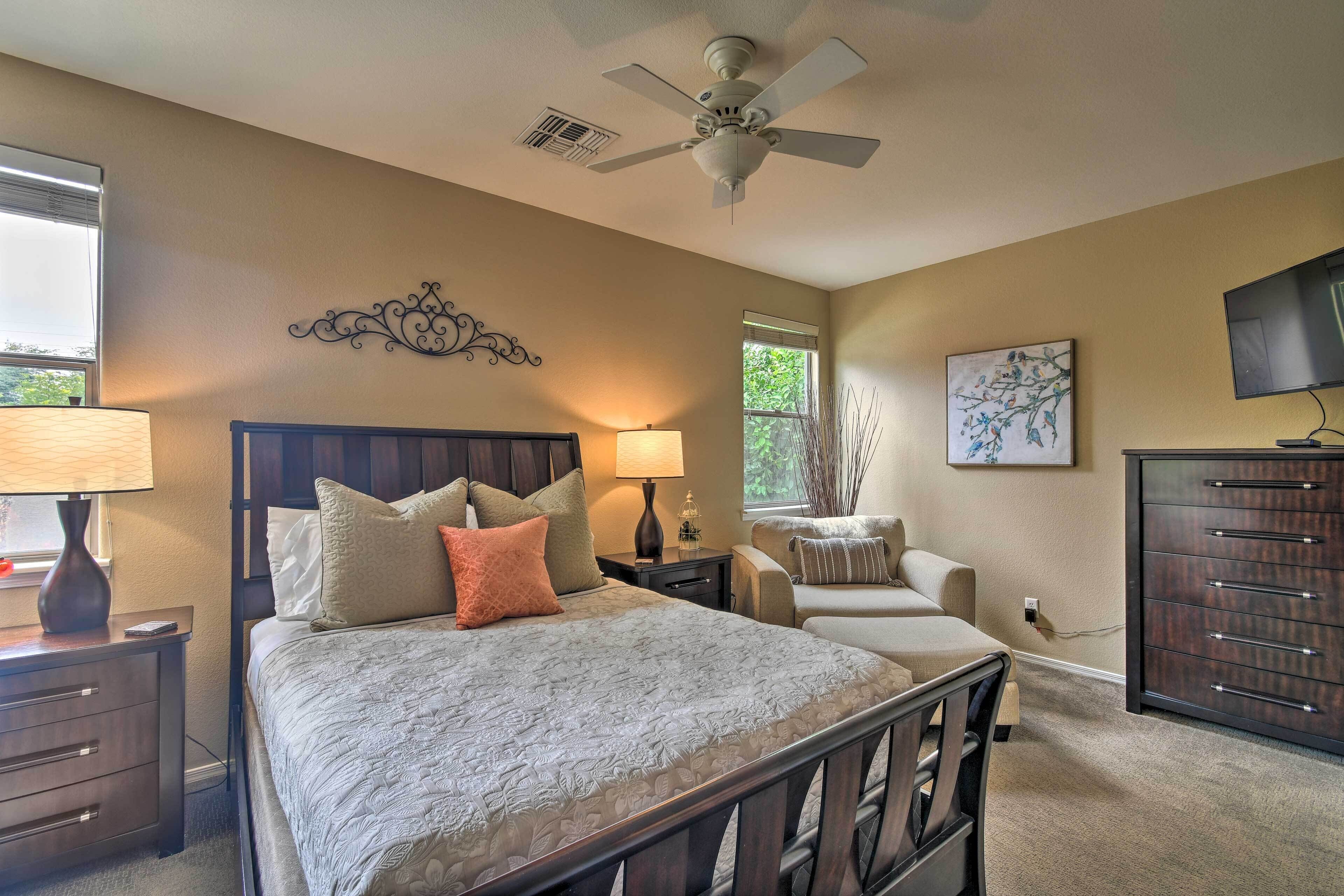 A bedroom with a bed, bedside tables, a chair, a dresser, a ceiling fan, and a TV.
